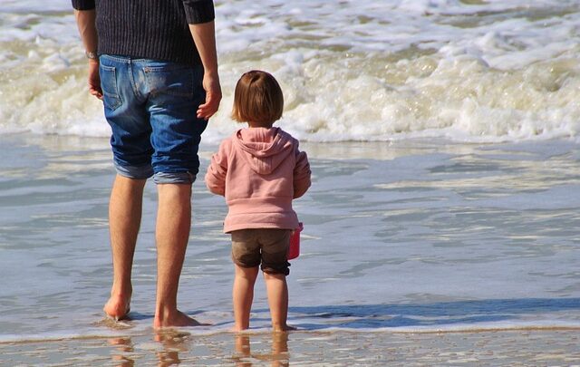 małe dziecko i rodzic na plaży brodzący w wodzie